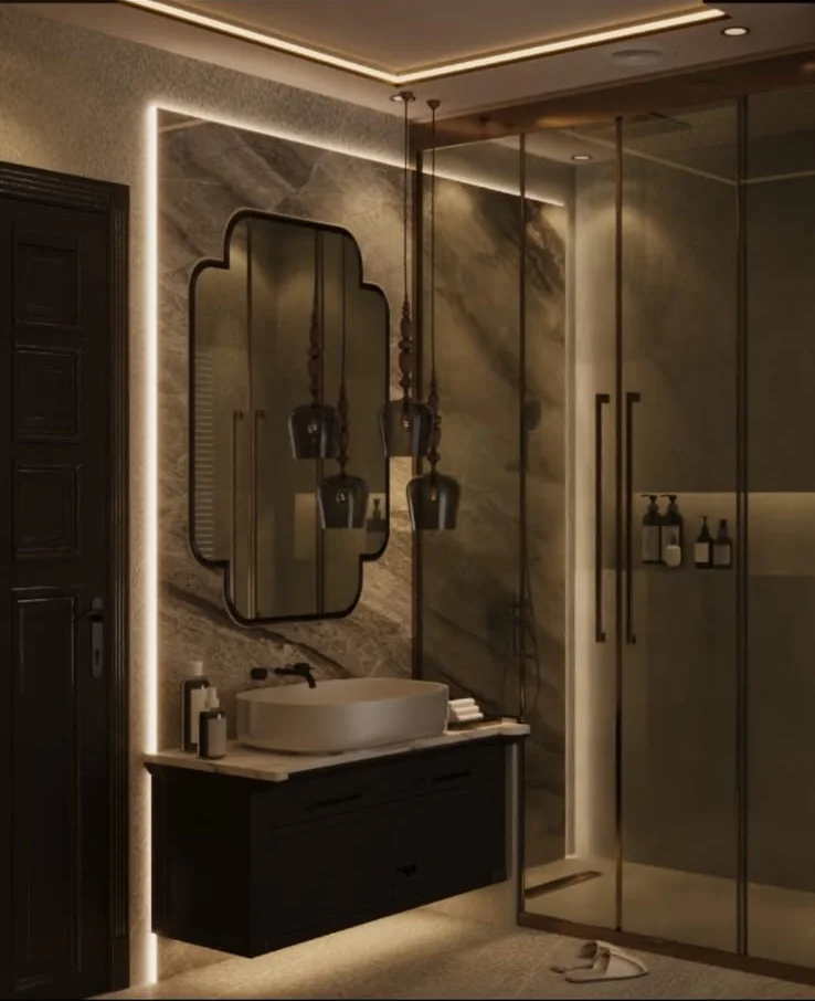 Dark bathroom with a full-height stone-clad vanity wall, vessel basin on a floating dark unit, shaped LED-frame mirror and glass shower enclosure