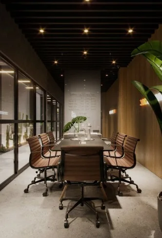 Compact boardroom with a dark conference table, tan leather rolling chairs, a black batten ceiling with spotlights and full-height glazed walls