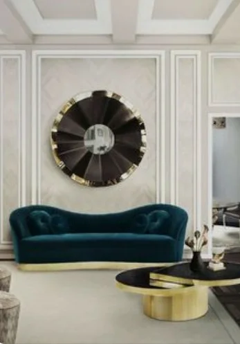 Luxury living room with a curved teal velvet sofa, a brass and black oval coffee table and a sunburst round mirror on panelled walls