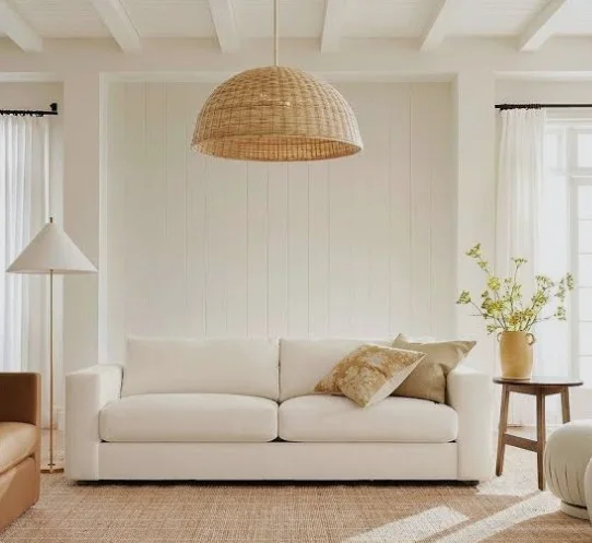 All-white living room with a cream sofa, a wicker dome pendant, shiplap-style wall panelling and natural-tone accessories