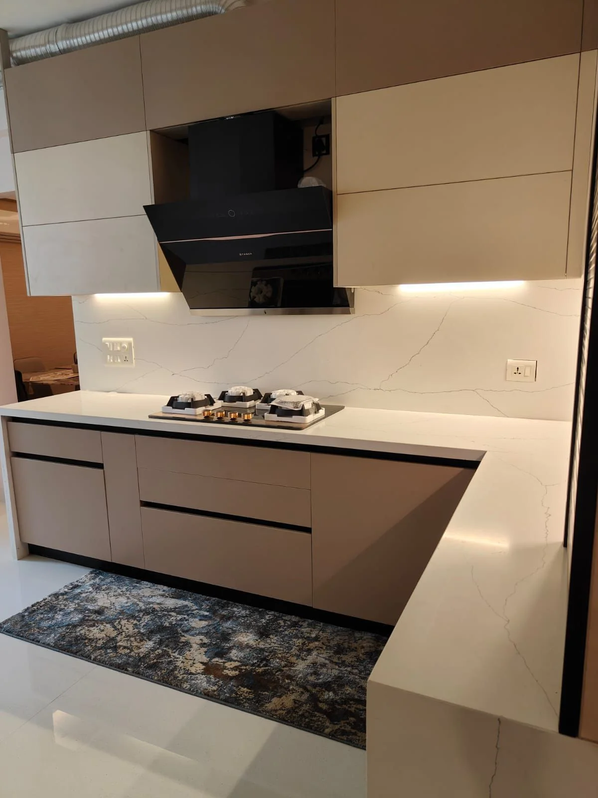 Handleless modular kitchen in taupe matte finish with a veined quartz backsplash and counter