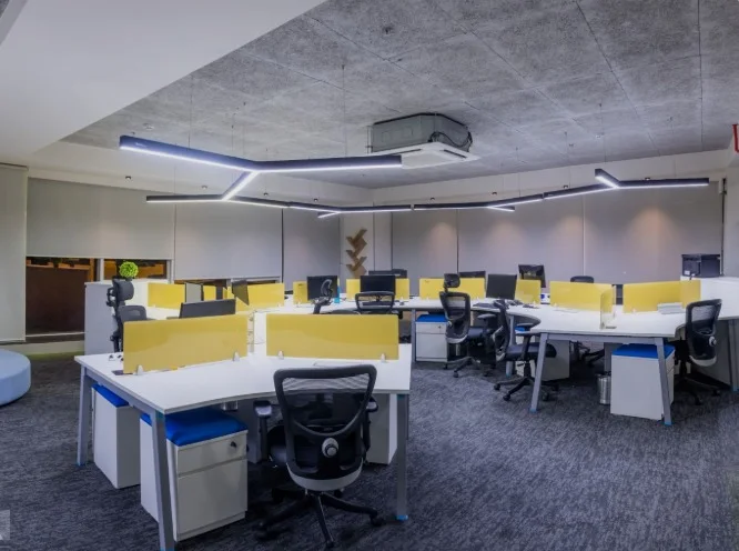 Open-plan office with white benching desks, acrylic screens and exposed concrete soffit